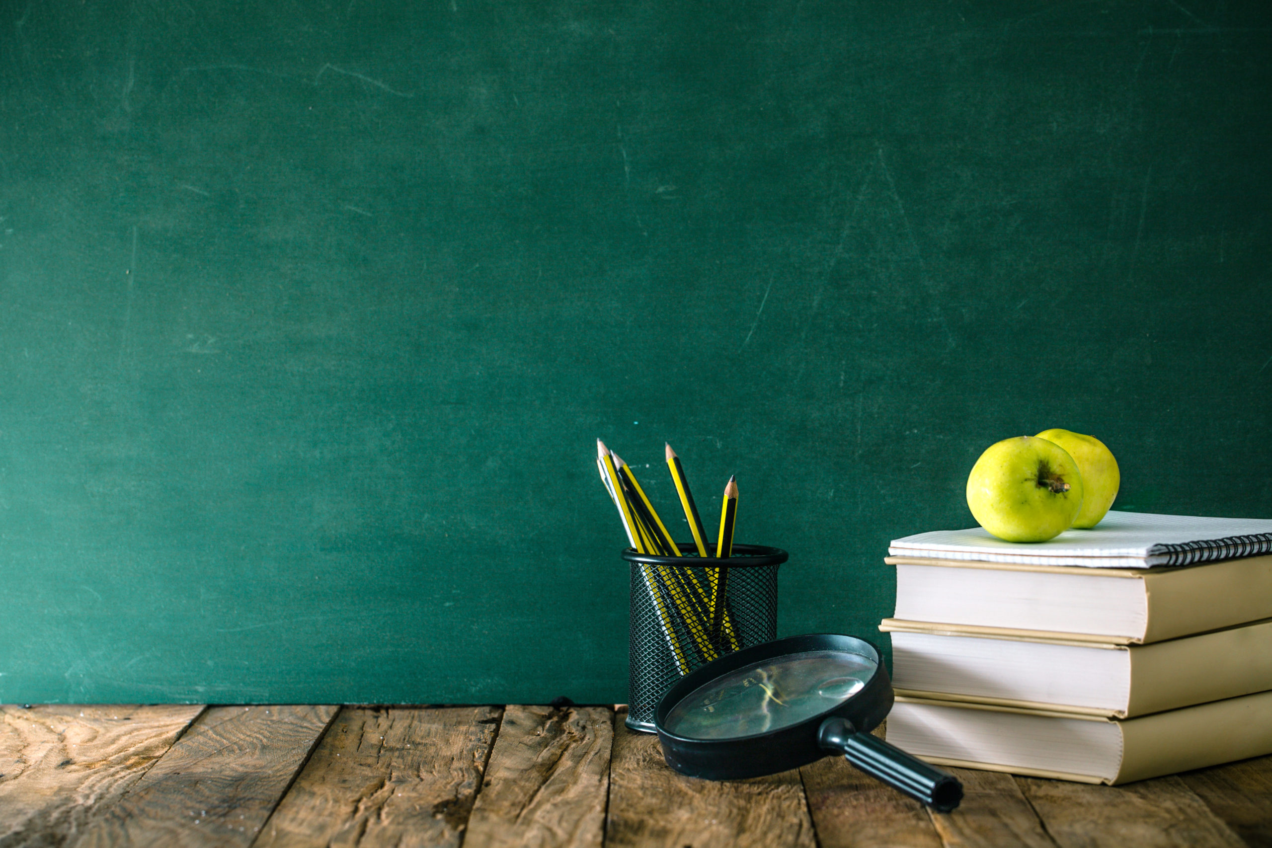 books and pencils on a desk by a chalkboard