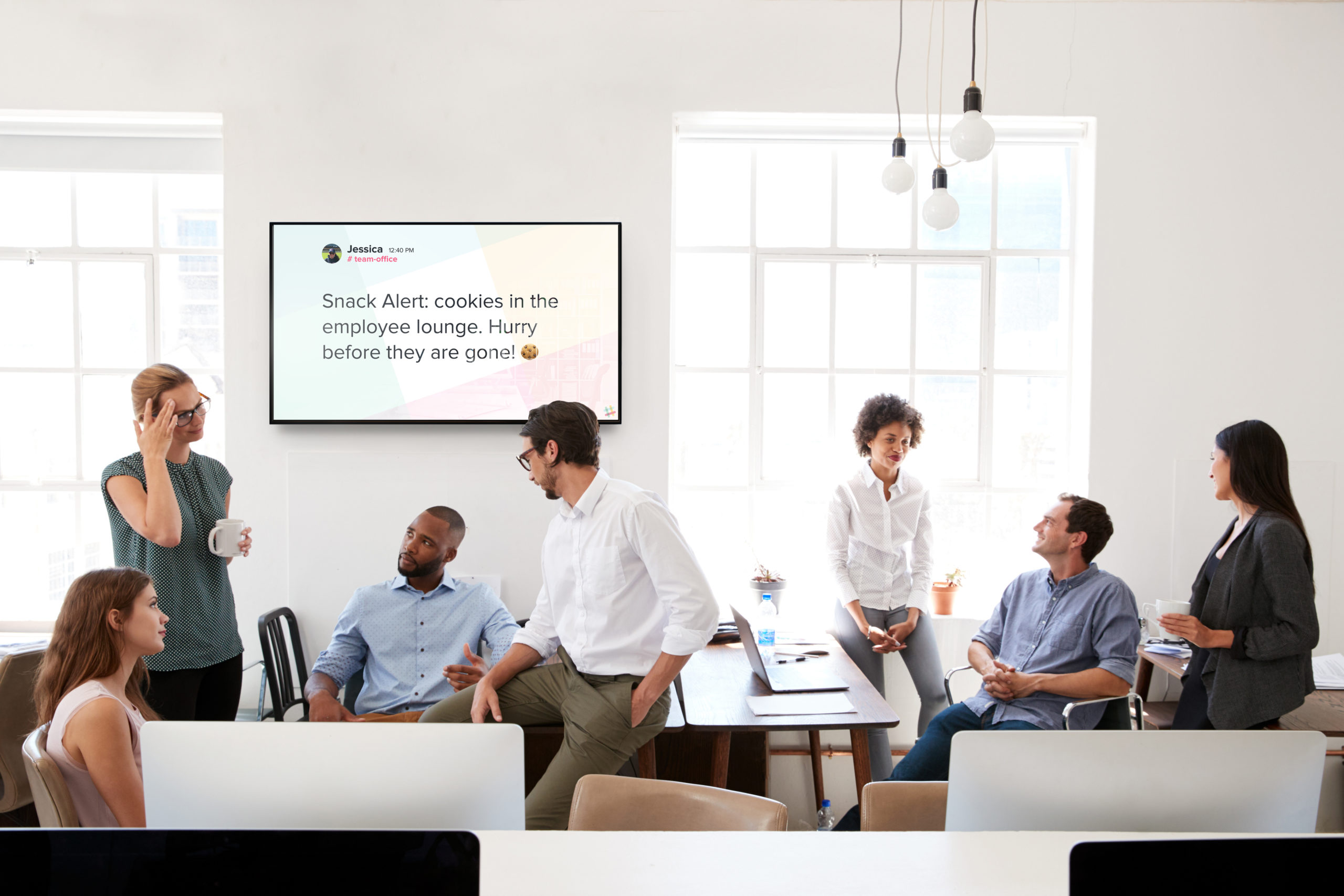 Team of diverse coworkers standing around table with digital signage for corporate communications on the wall behind them