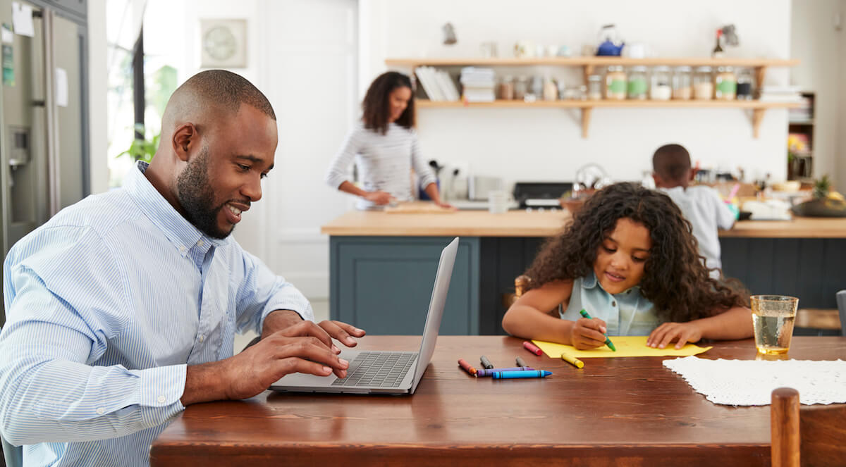 man working at home on kitchen table with daughter and wife in the room