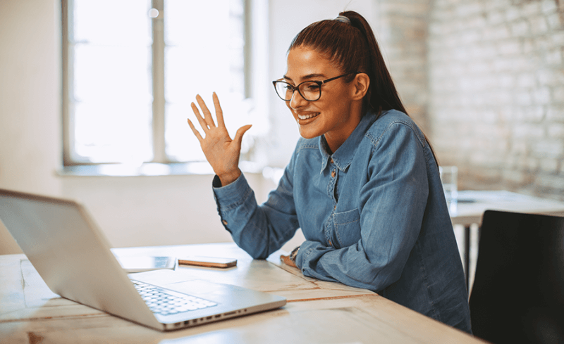 Remote employee in home office waving at manager on her computer screen