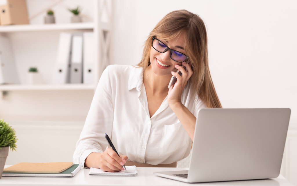 Remote employee on phone while writing in front of laptop