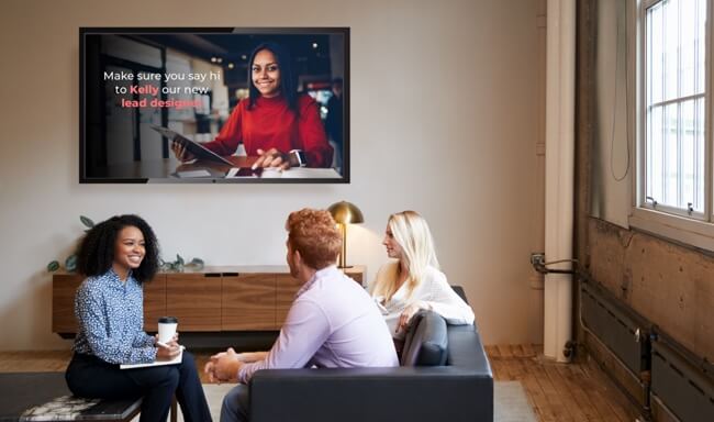 workers sitting around couches under a display discussing