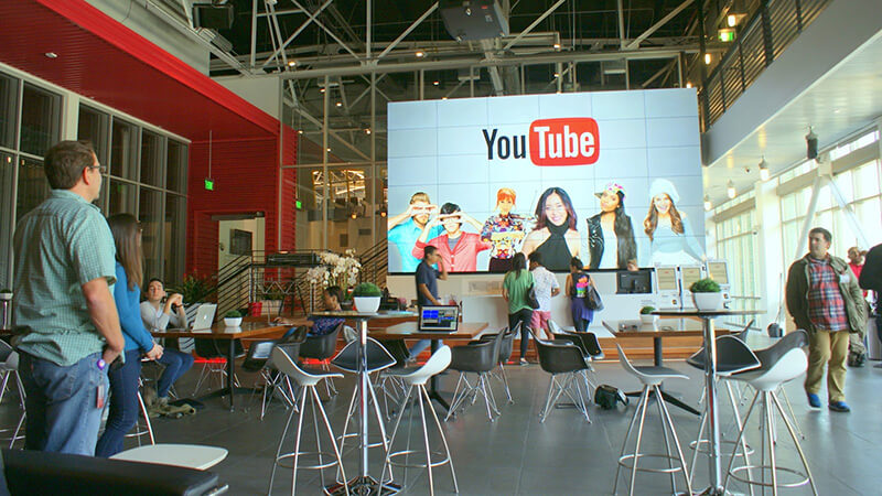 group of people inside a large room with a large screen display showing a youtube logo