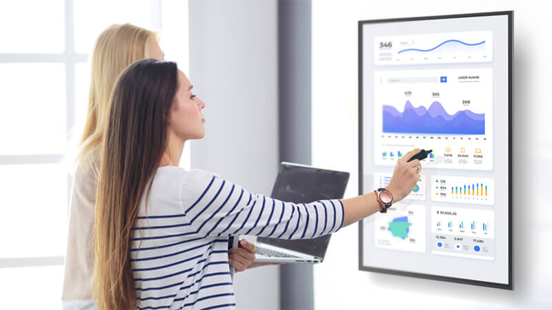 Two coworkers looking at a business dashboard on a digital display