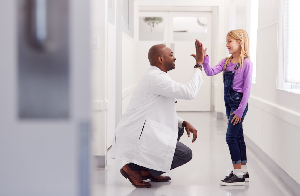Doctor gives a young patient high five in hospital corridor
