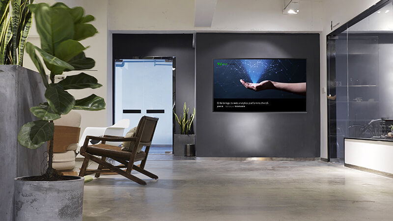 A digital signage screen in a modern office lobby displaying a news feed