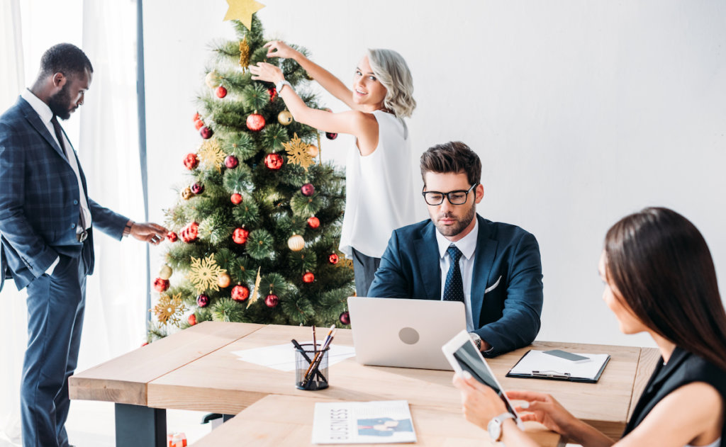 woman decorating a christmas tree in office with employees