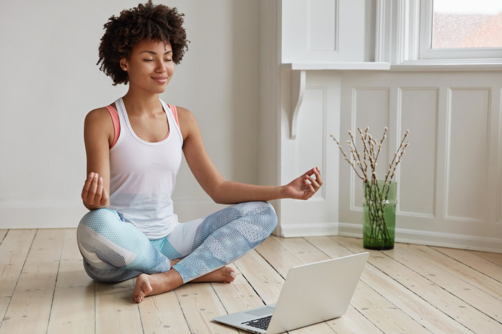 woman doing yoga while her laptop is in front of her on the floor
