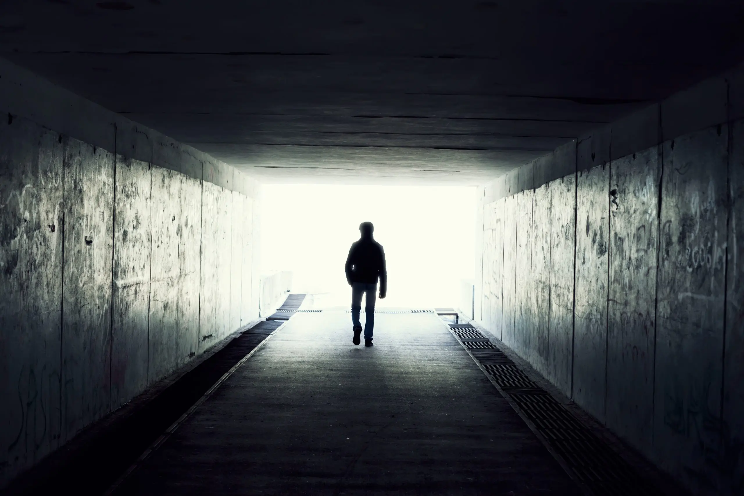 Person walking towards light through a dark tunnel